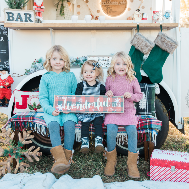 Photo of 3 kids sitting in front of the Wandering Jade Trailer with Christmas Decorations.